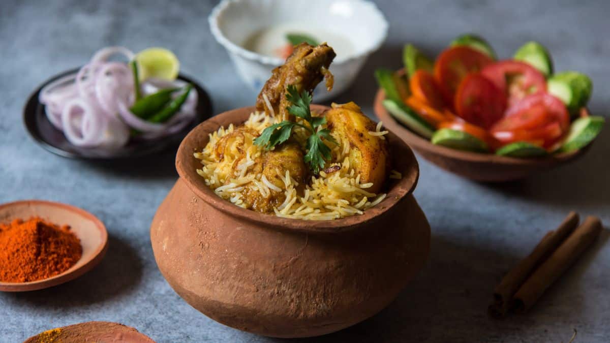 Mughlai chicken biryani in a clay pot with raita and onion in the background.