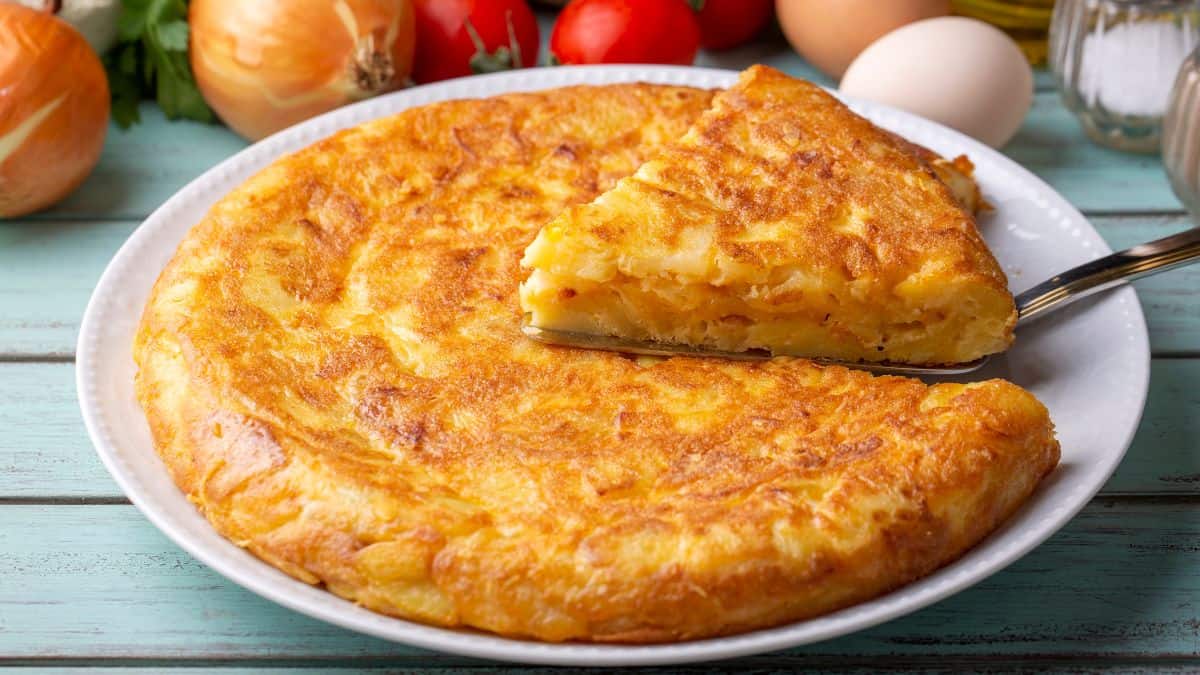 Spanish omelet on a white plate with onions in the background.