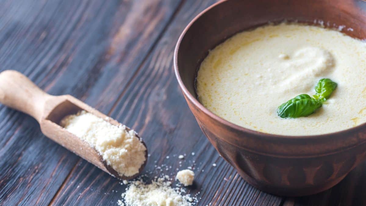 Alfredo sauce in a brown bowl with cheese in the background.