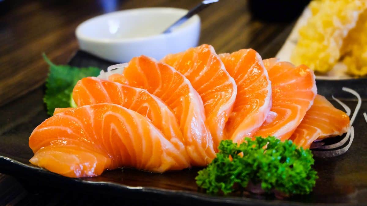 Sashimi on a plate with dip in the background.