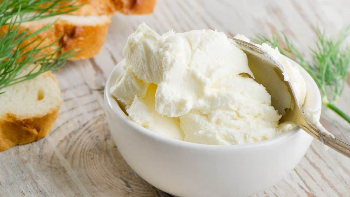 A bowl of cream cheese with slices of bread in the background.