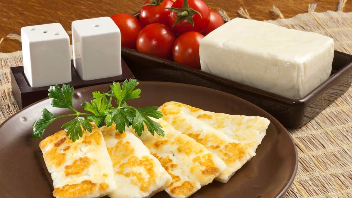 Grilled halloumi on a plate with a block of fresh halloumi in the background.