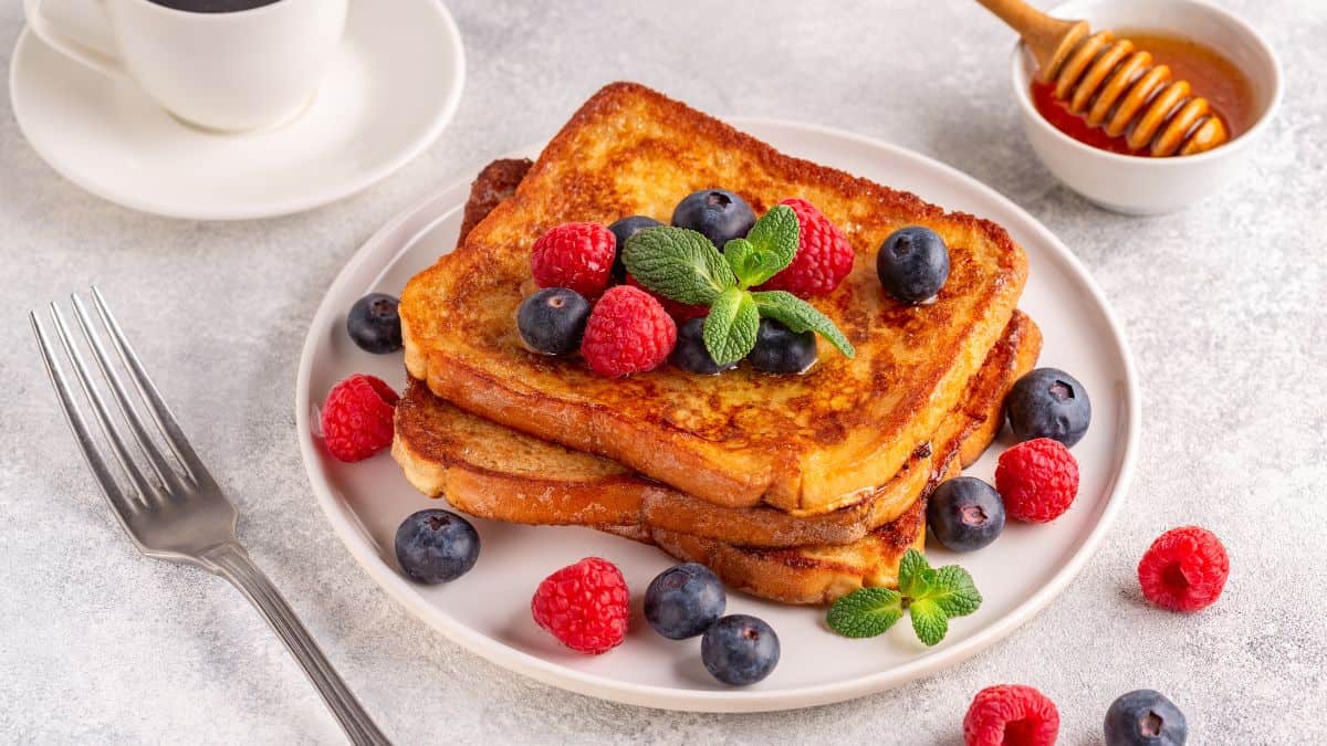 French toast on a white plate topped with fresh berries.