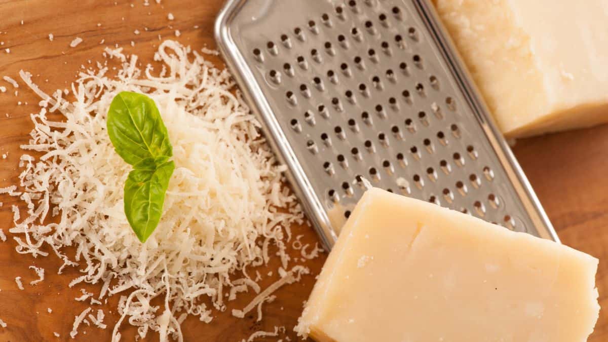 Grated and block of parmesan cheese on a wooden board.