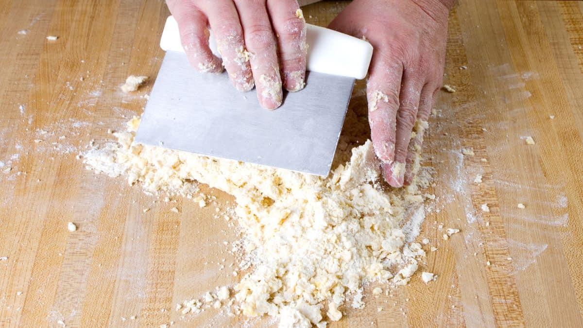 Person gathering dough using dough scraper.