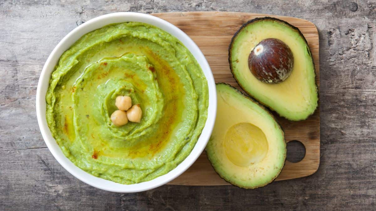 Avocado hummus in a white bowl with avocado in the background.