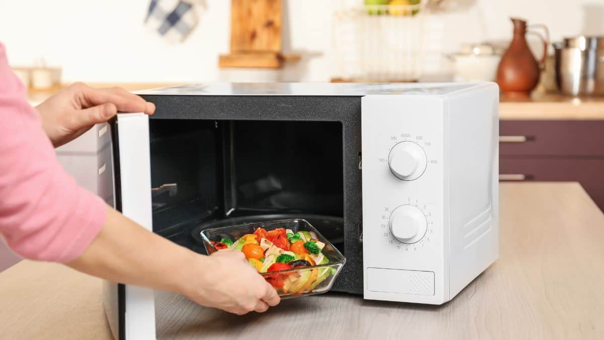 Woman placing vegetables in microwave.