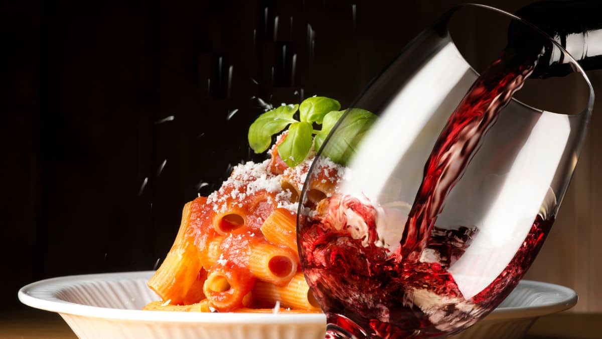 Wine being poured in a glass with pasta in the background.