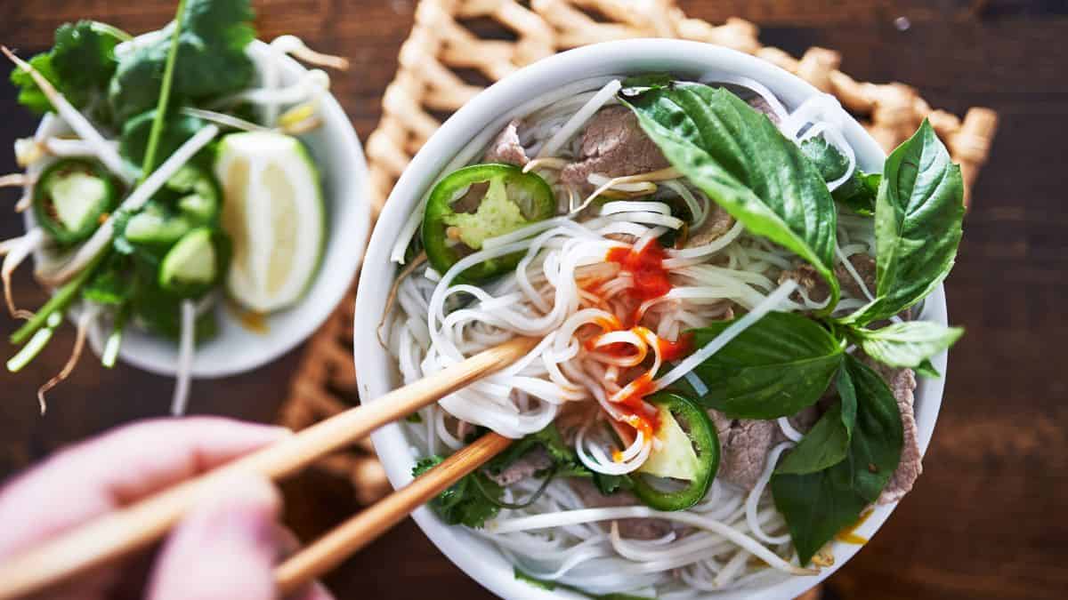 Pho in a bowl with a person with chopsticks.