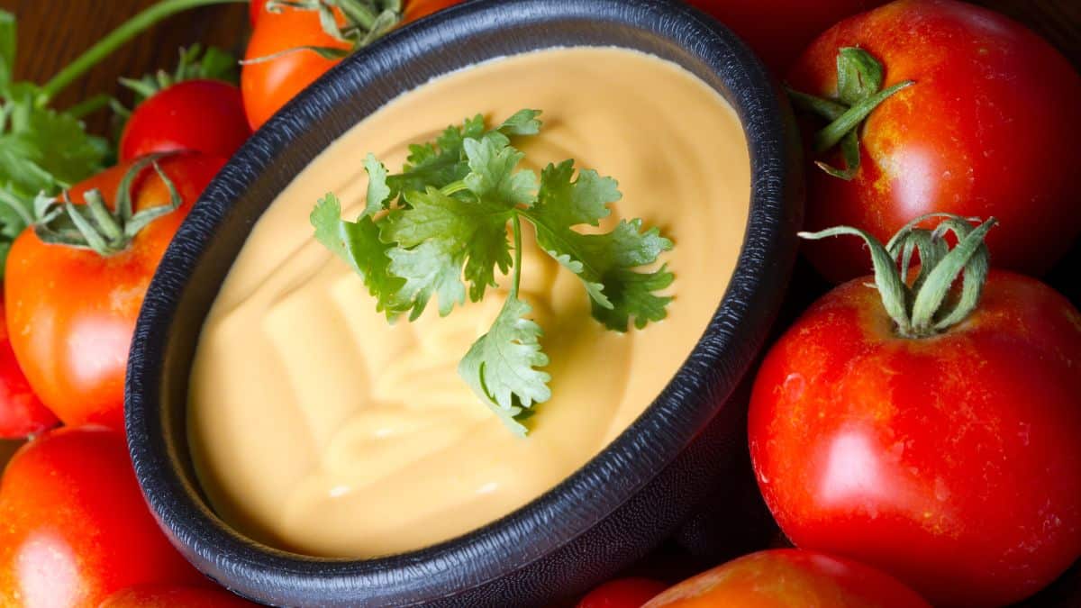 Queso sauce in a black bowl with tomatoes in the background.