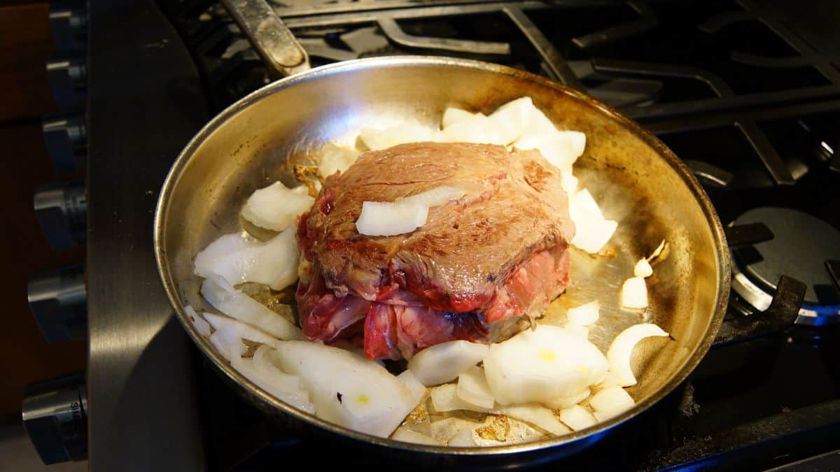 Meat being braised in a pan.