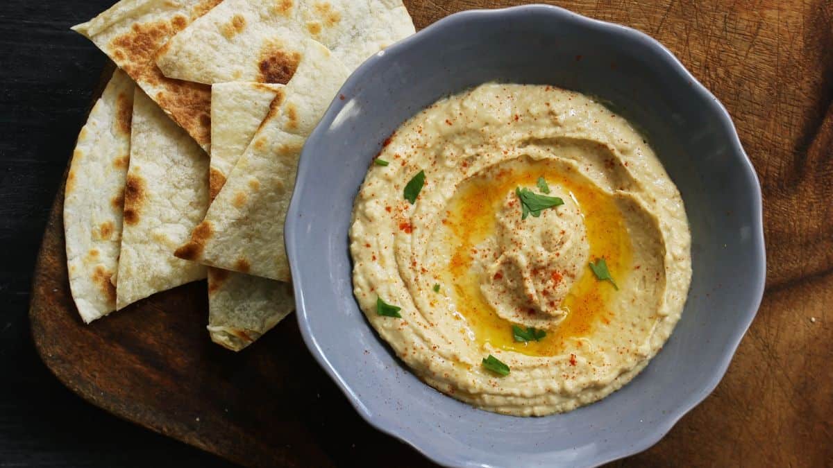 Spicy hummus in a grey bowl with pita bread in the background.