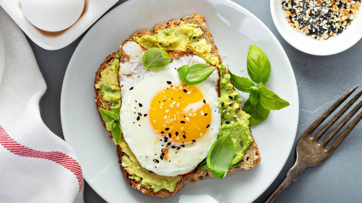 Avocado toast topped with egg on a white plate.