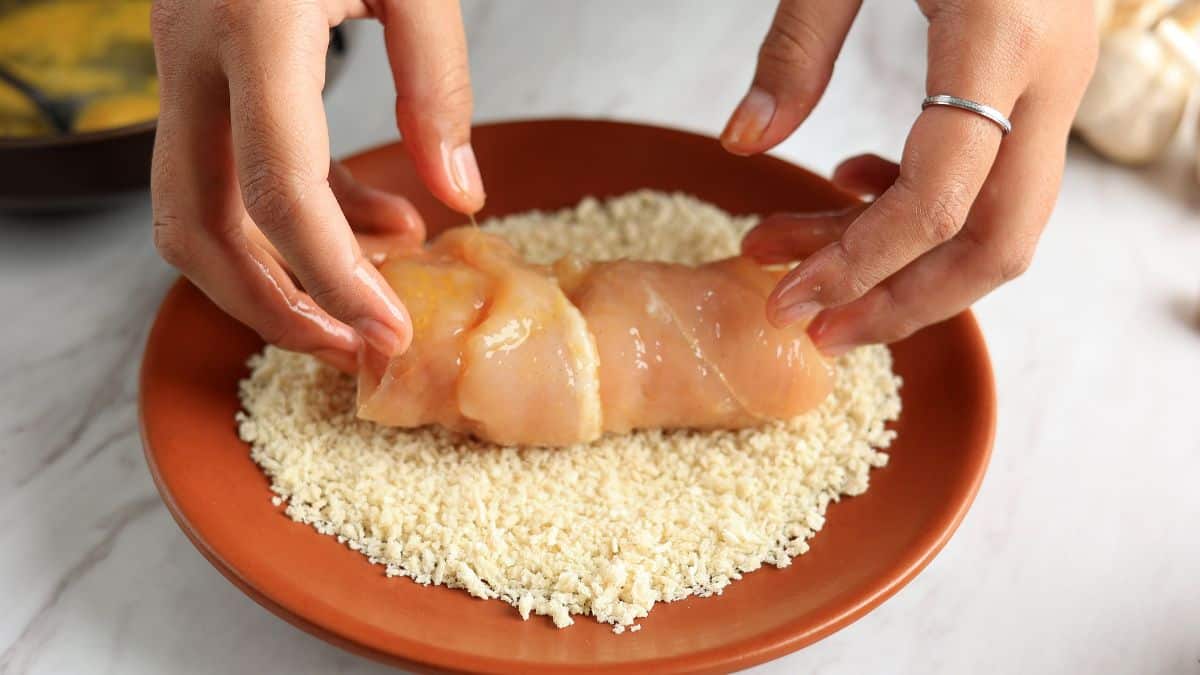 Chicken being coated in breadcrumbs.