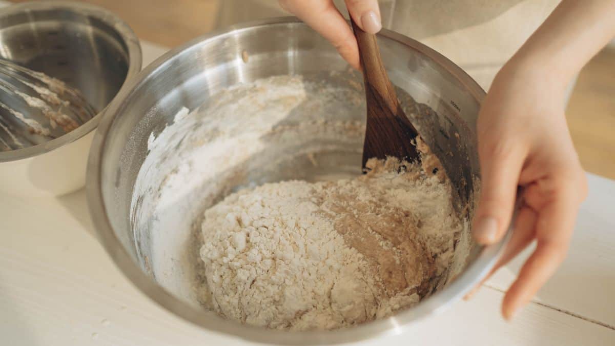 Person mixing dough in a large bowl.