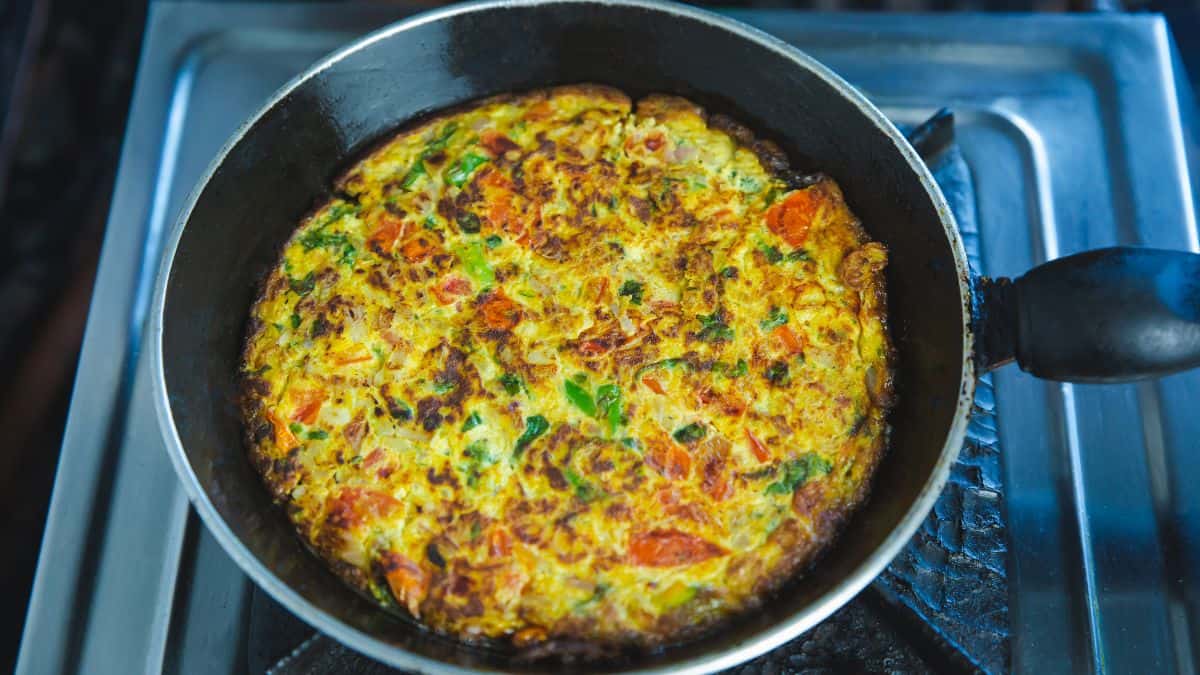 Masala omelet cooked in a skillet on stovetop.