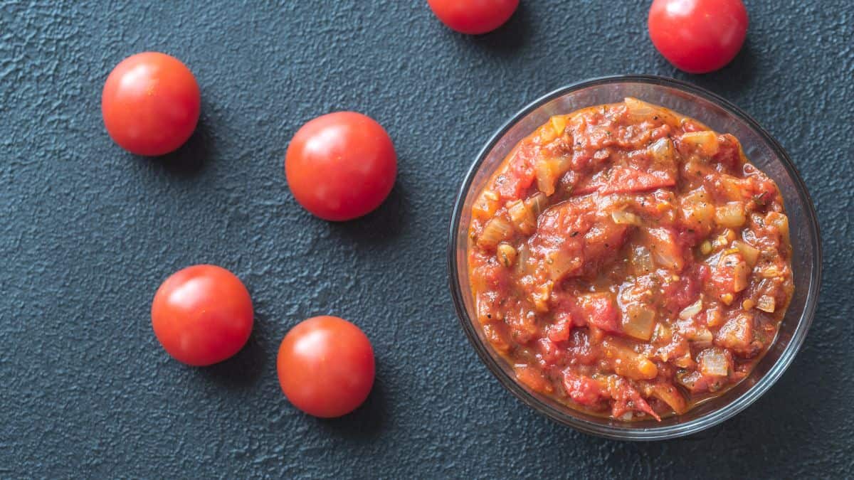 Arrabbiata sauce in a bowl with tomatoes in the background.