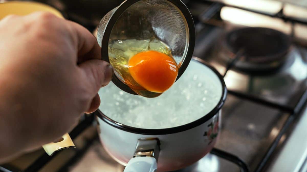 Egg being poured in boiling water for poaching.