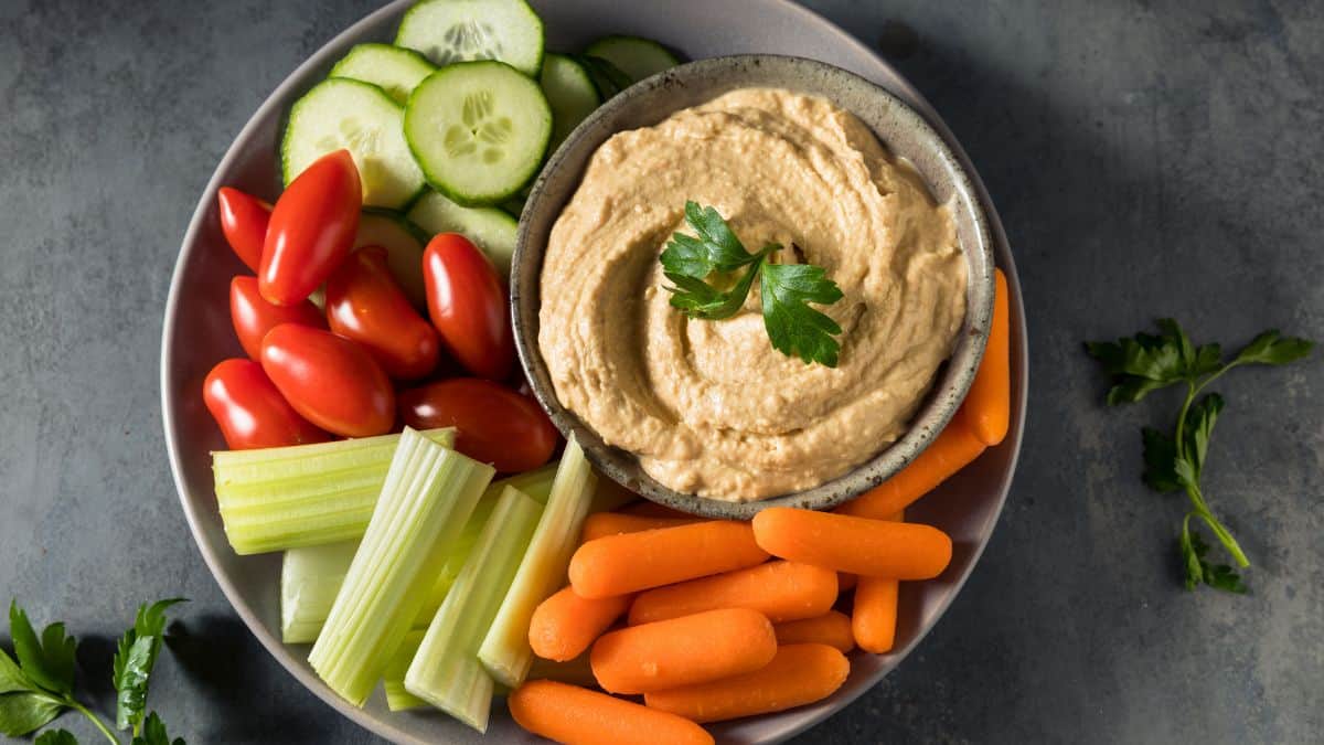 A bowl of spicy hummus served with dippers.