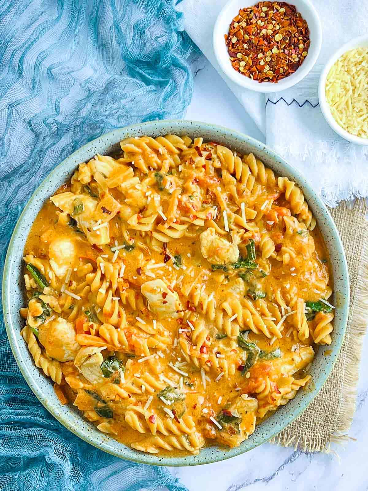 Chicken chickpea pasta in a bowl with chili flakes and cheese in the background.