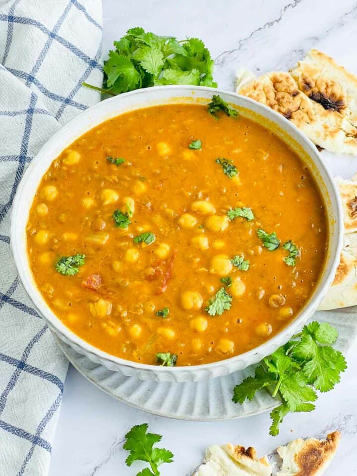 Chickpea lentil curry in a white bowl served with naan.