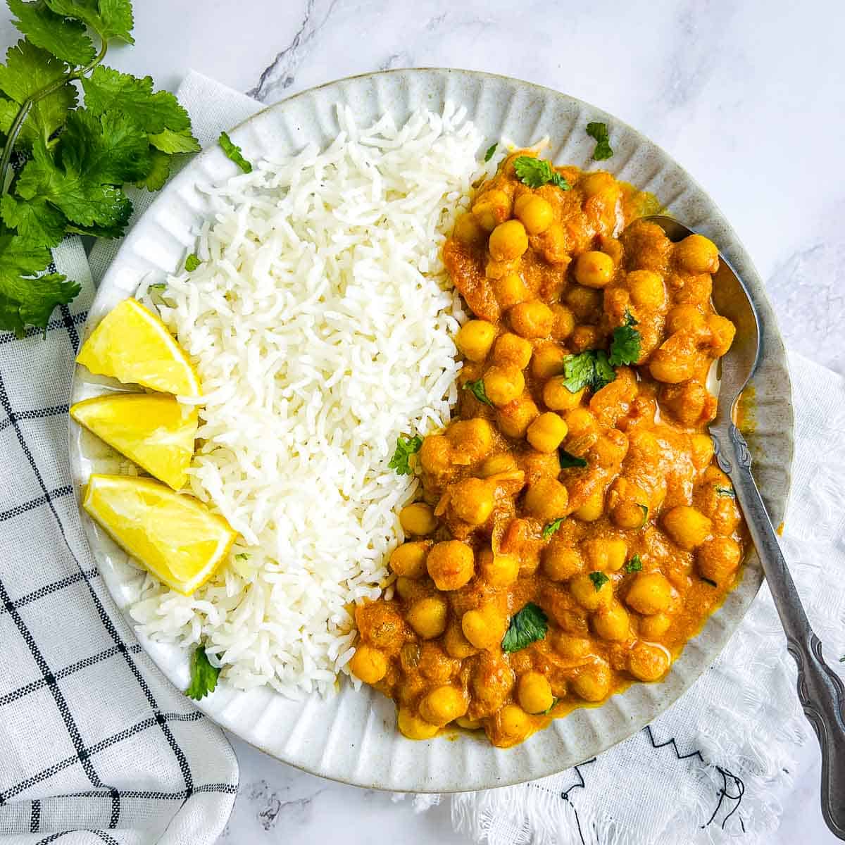 Chickpea mango curry and rice on a white plate with lemon wedges on the top.