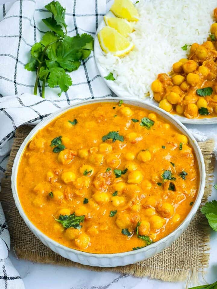 Chickpea mango curry in a white bowl with rice plate in the background.