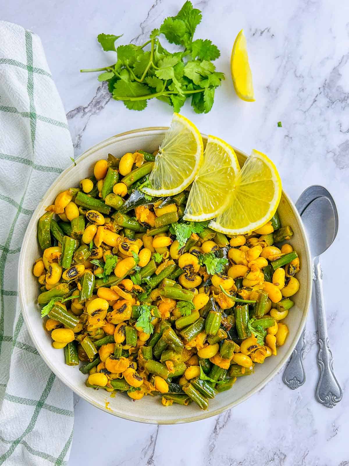 Green beans and black-eyed peas stir fry in a white bowl garnished with lemon wedges.