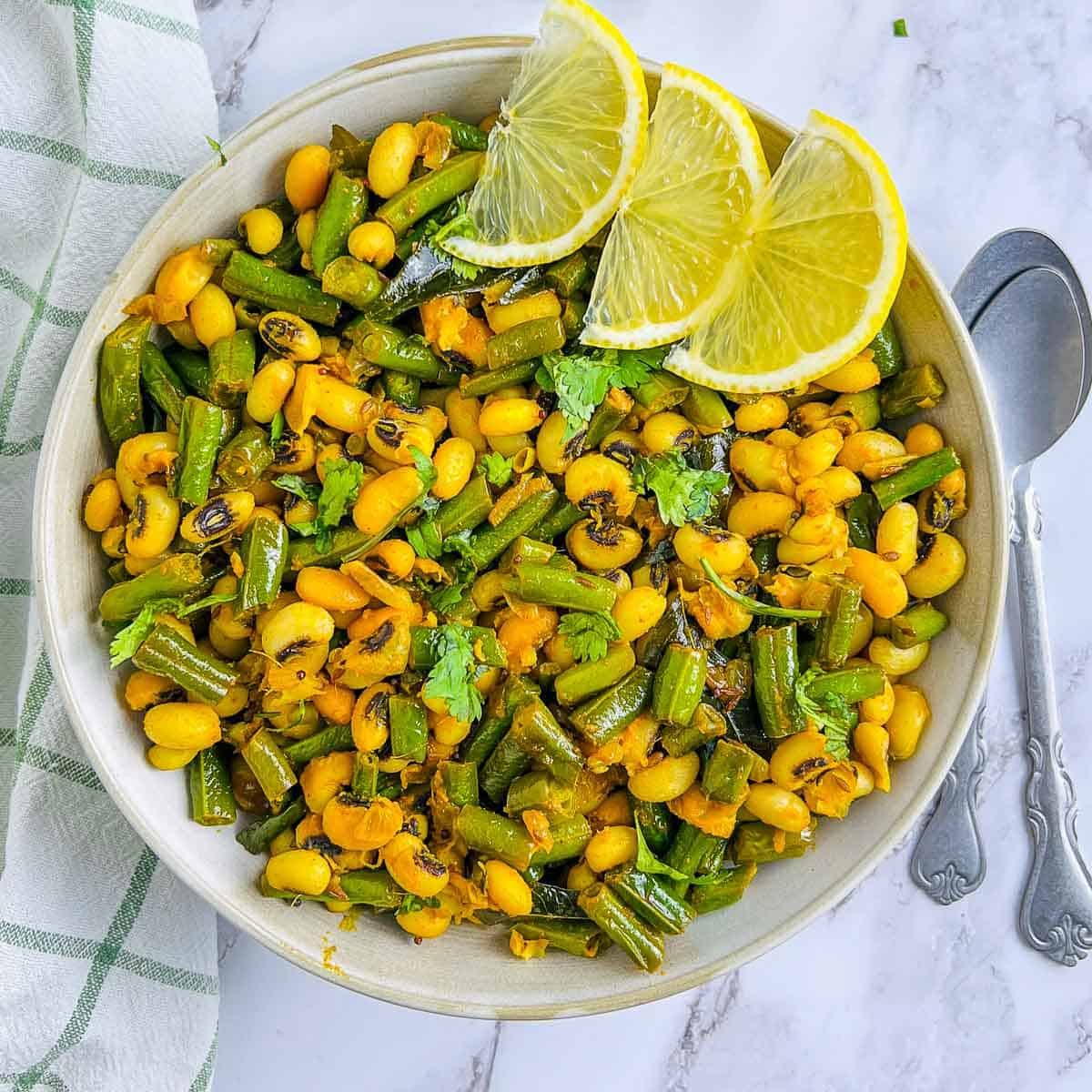 Green beans and black-eyed peas stir fry with spoons in the background.