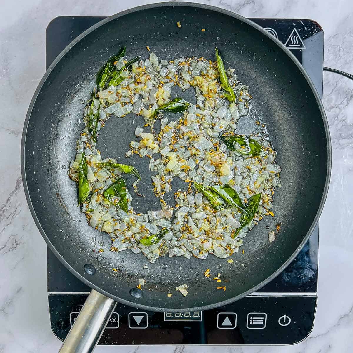 Sauteed onion, ginger, garlic, and curry leaves in a frying pan.