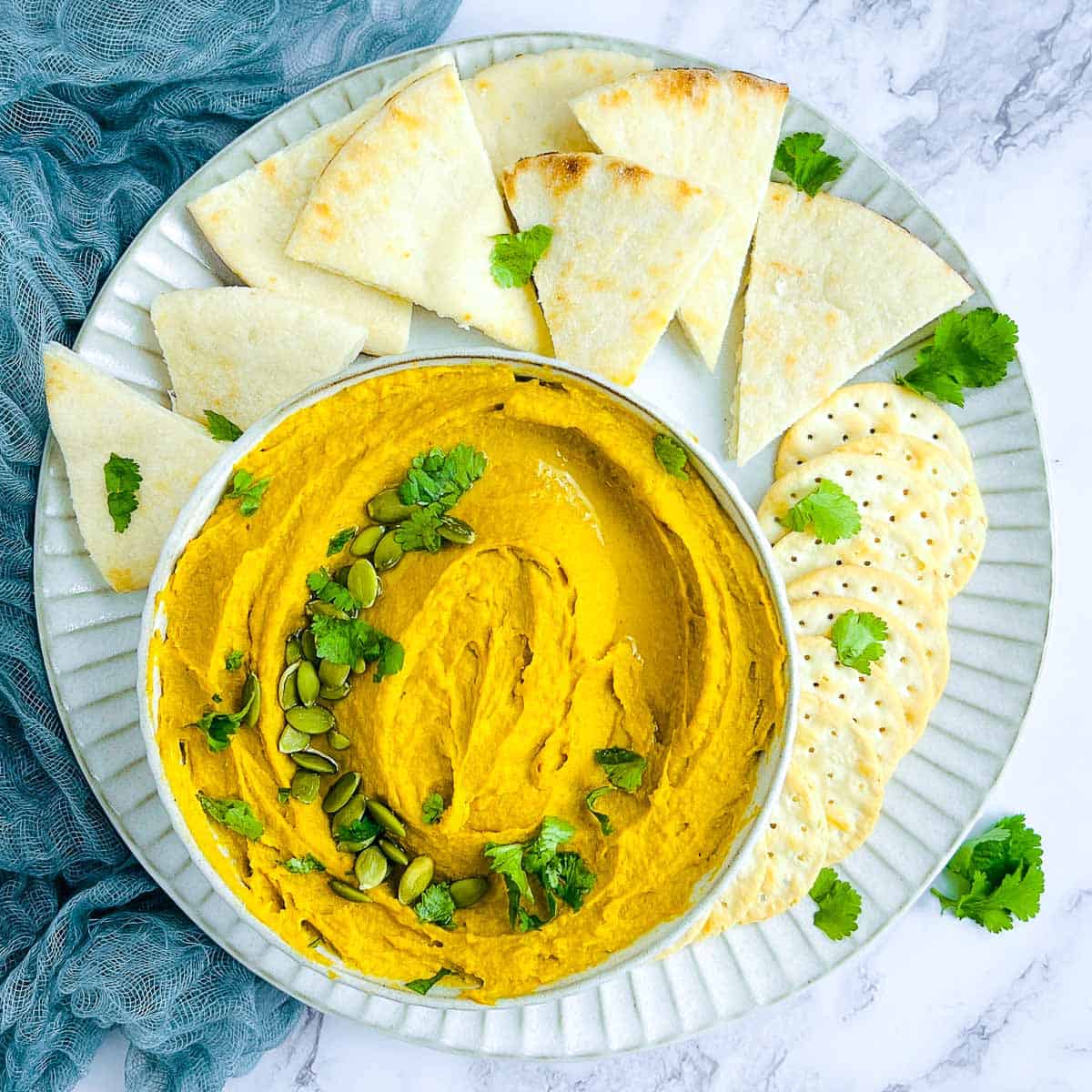 Pumpkin black garlic hummus in a white bowl garnished with cilantro and pumpkin seeds.