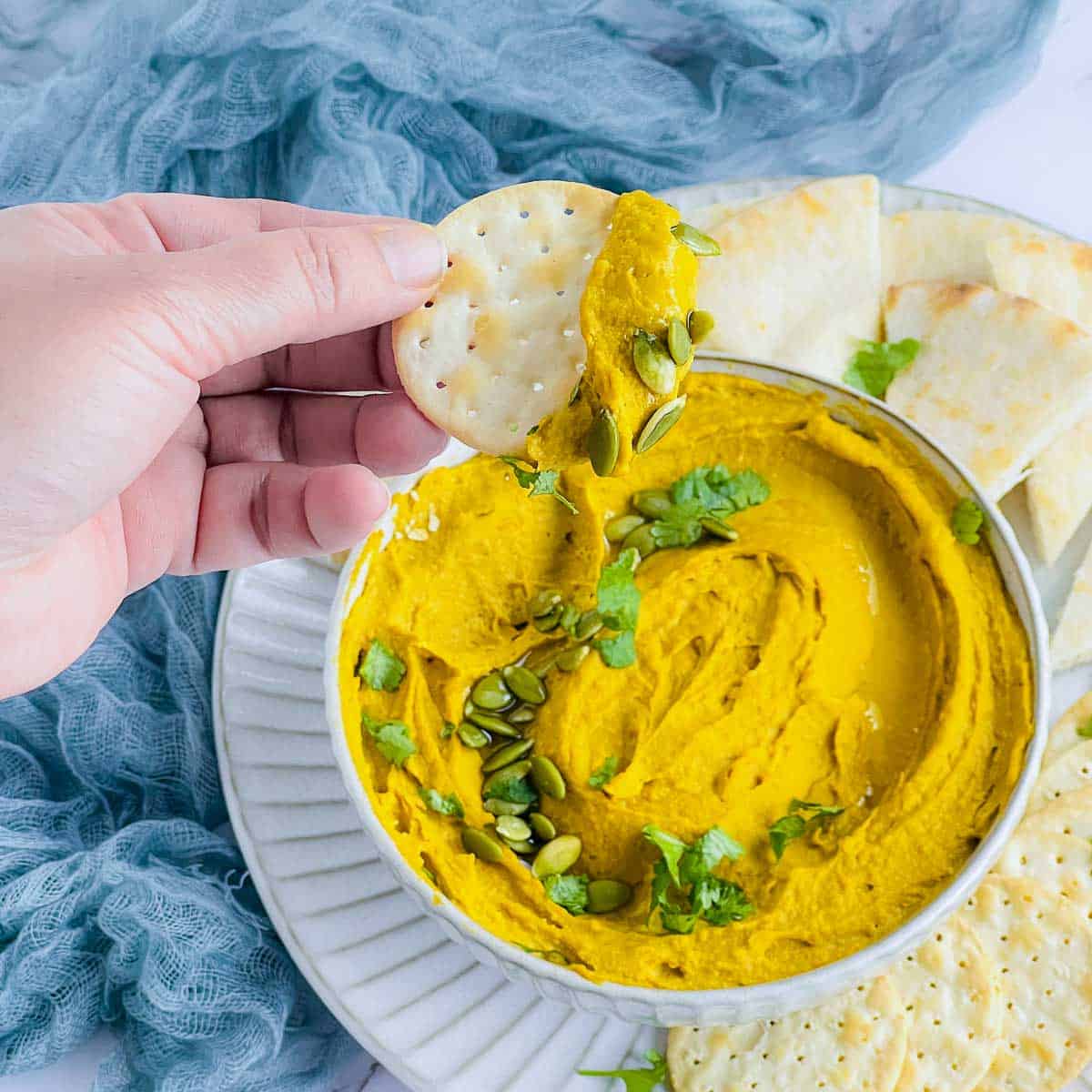 A cracker dipped into the hummus bowl.