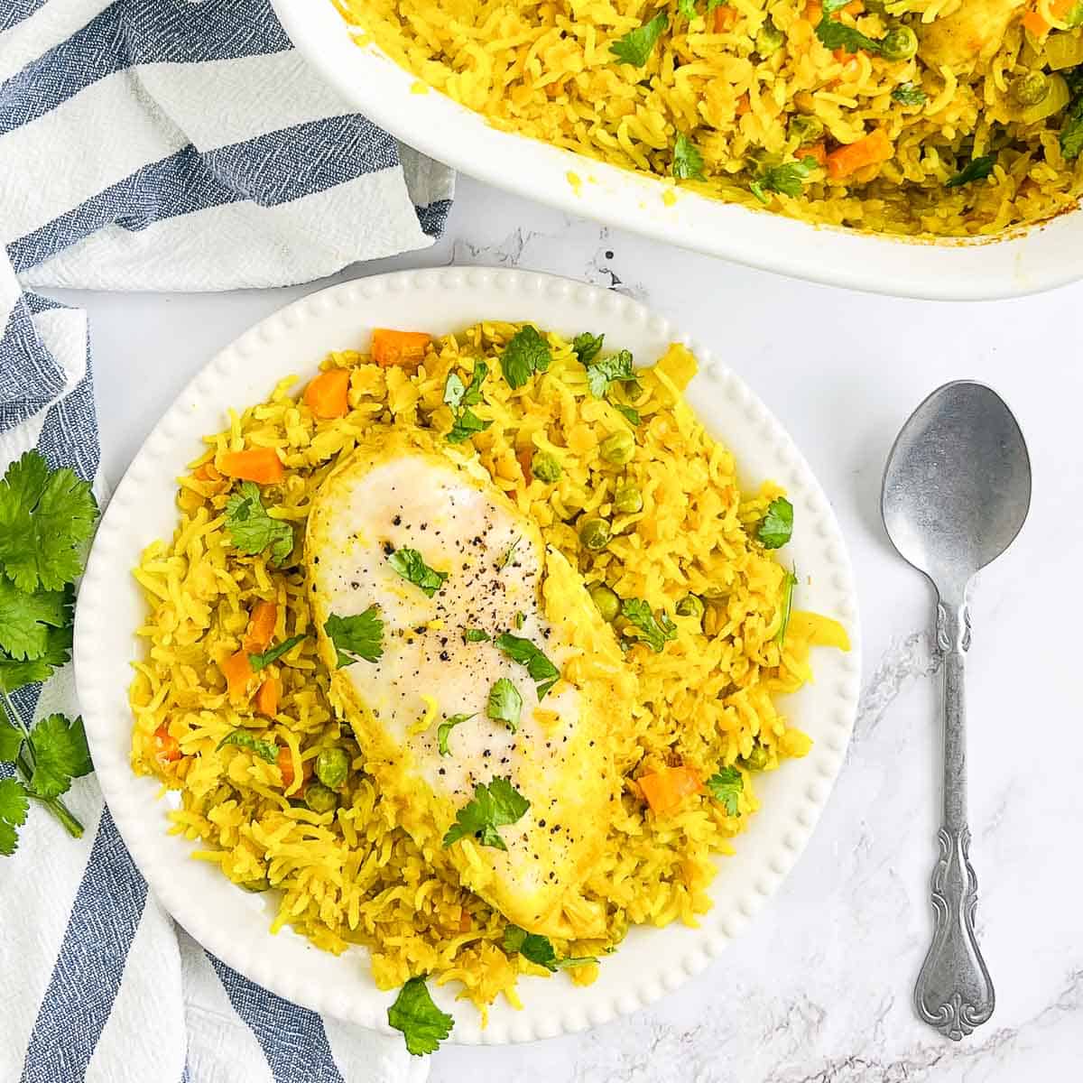 Turmeric rice casserole on a a white plate with casserole dish in the background.