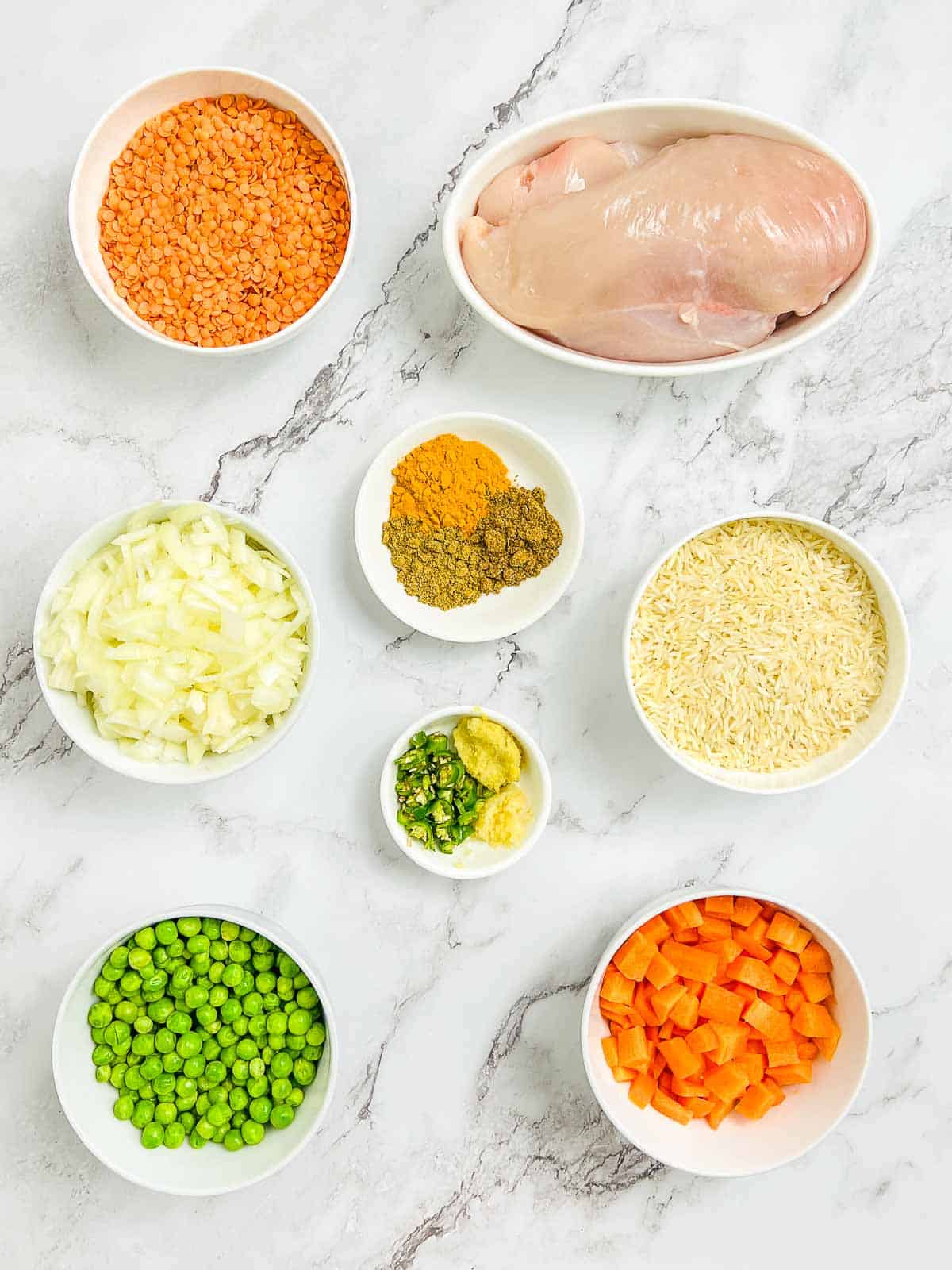 Ingredients to make turmeric chicken and rice casserole on a marble surface.