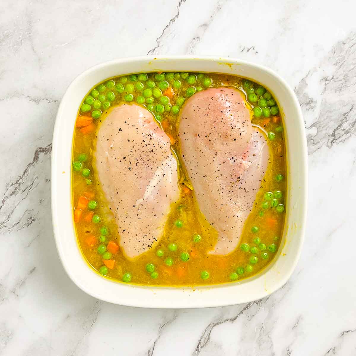 Broth and chicken added to the dish before covering and baking.