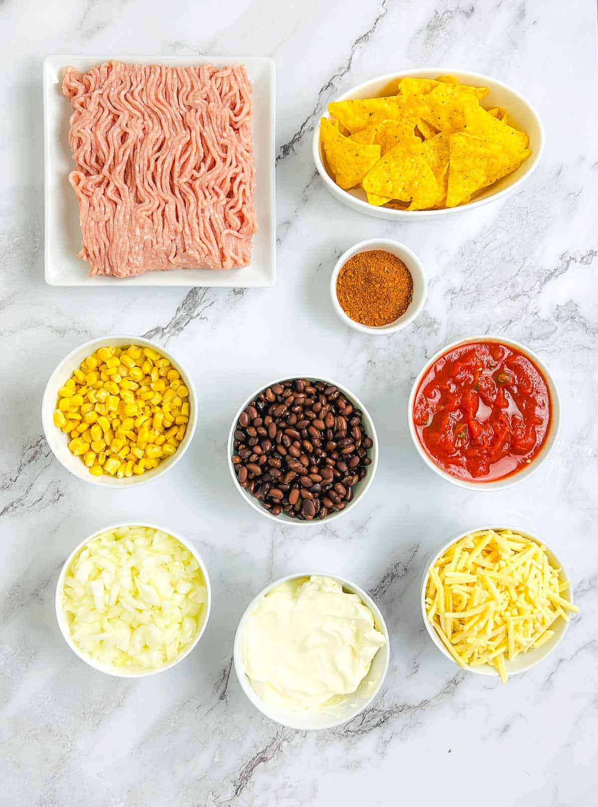 Ingredients to make walking taco casserole on a marble surface.