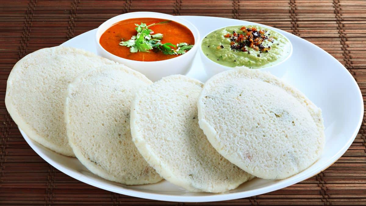 Idlis on a white plate served with sambar and chutney.