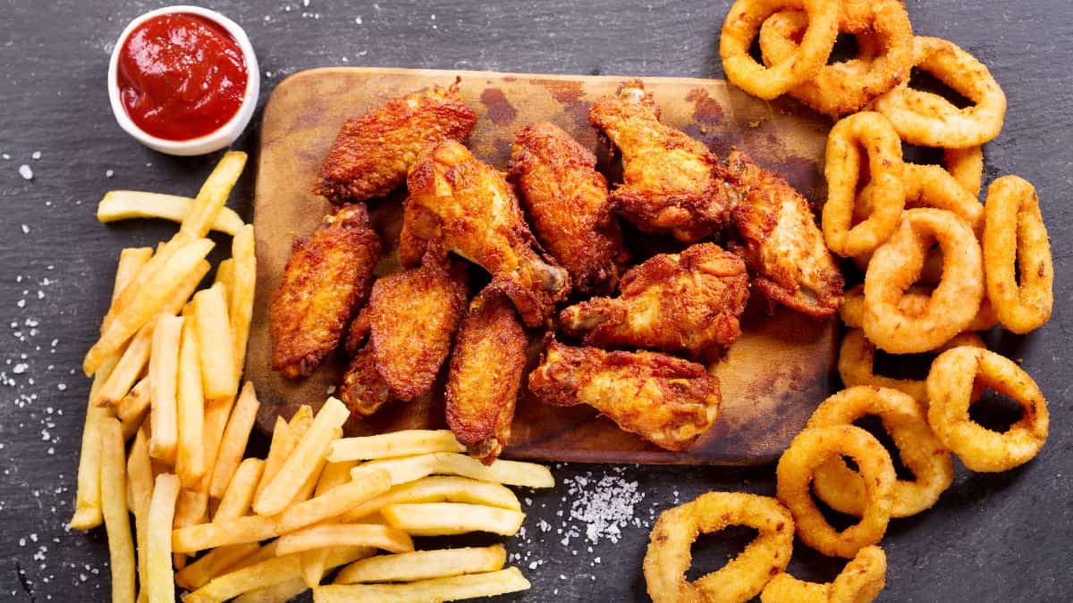 Chicken wings, onion rings, and fries on a wooden board.