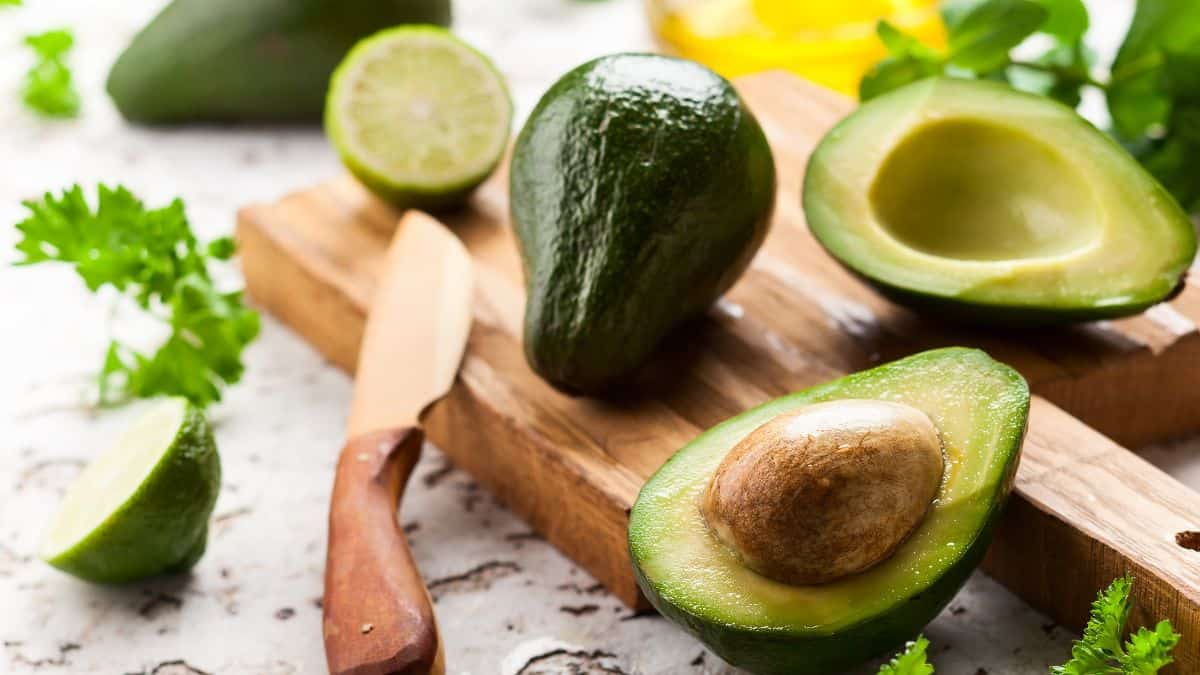 Whole and cut avocado on a wooden board.