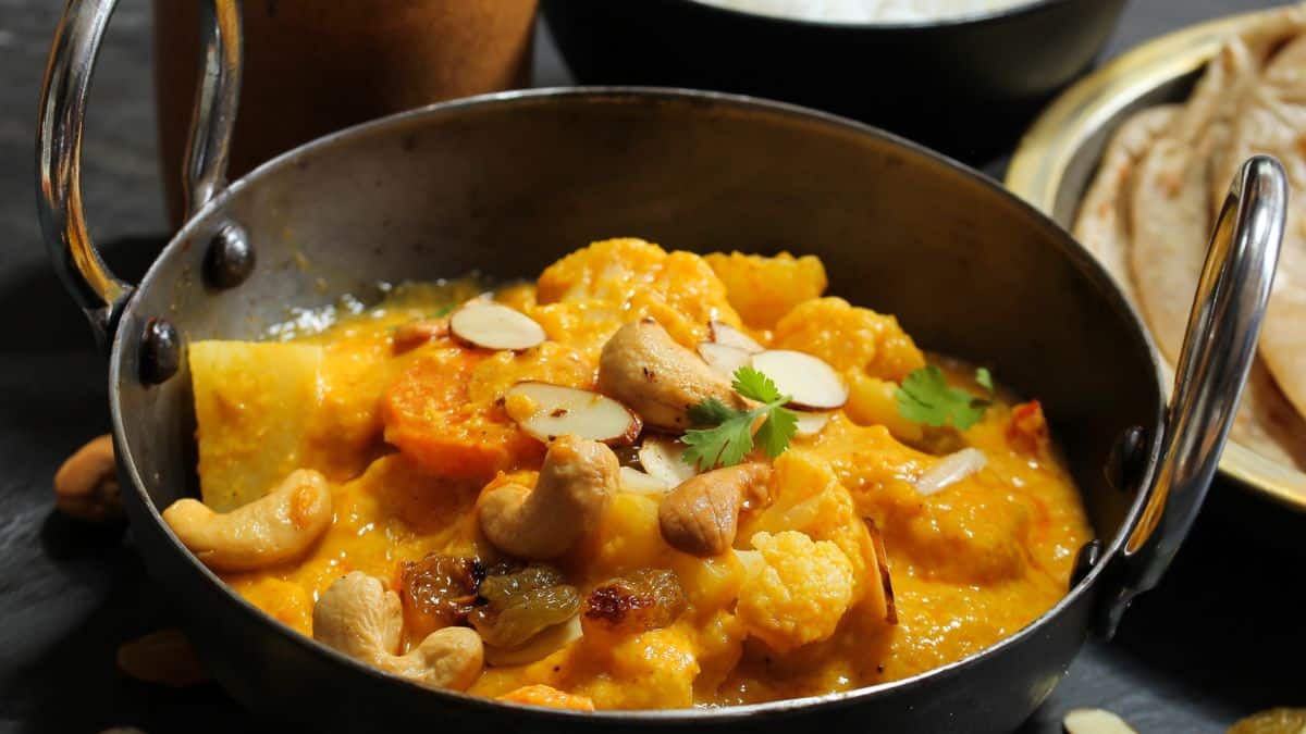 Vegetable korma served in a small kadhai with naan in the background.