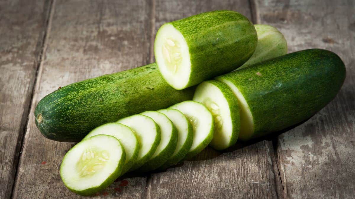 Whole and cut cucumber on a wooden board.