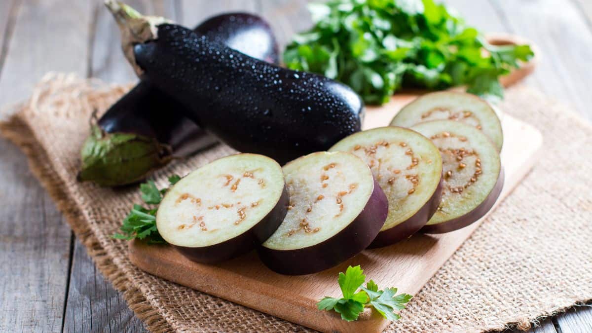 Whole and sliced Italian eggplant on a wooden board.