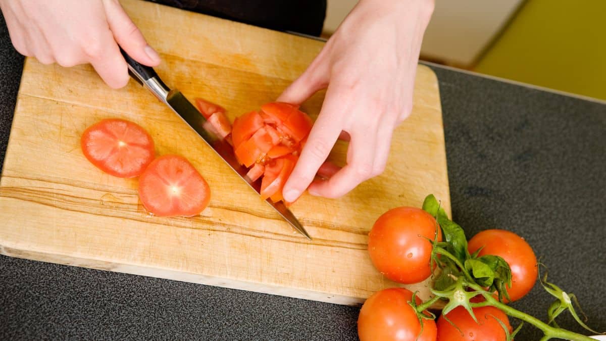 Woman chopping tomatoes on a cutting board.