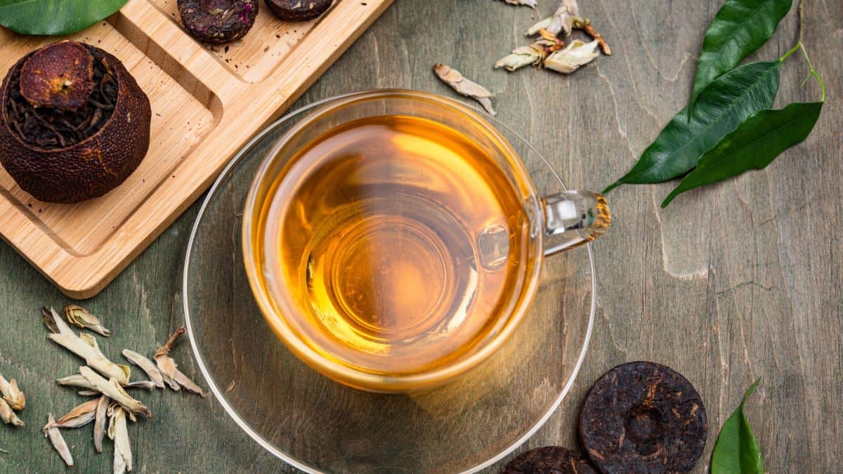 Chinese pu erh tea in a cup with tea leaves in the background.