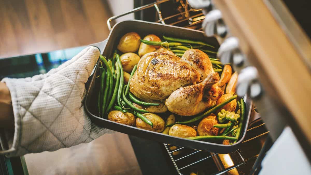 Person taking out roast chicken from the oven.