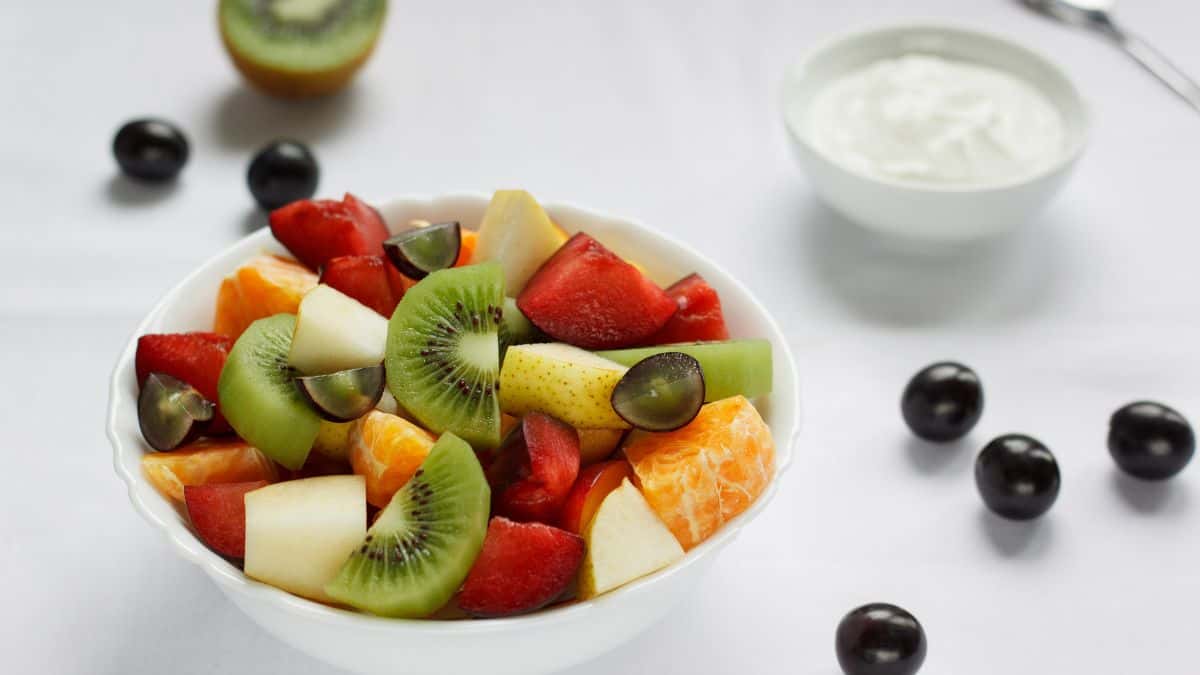 A bowl of fruit salad with yogurt in the background.