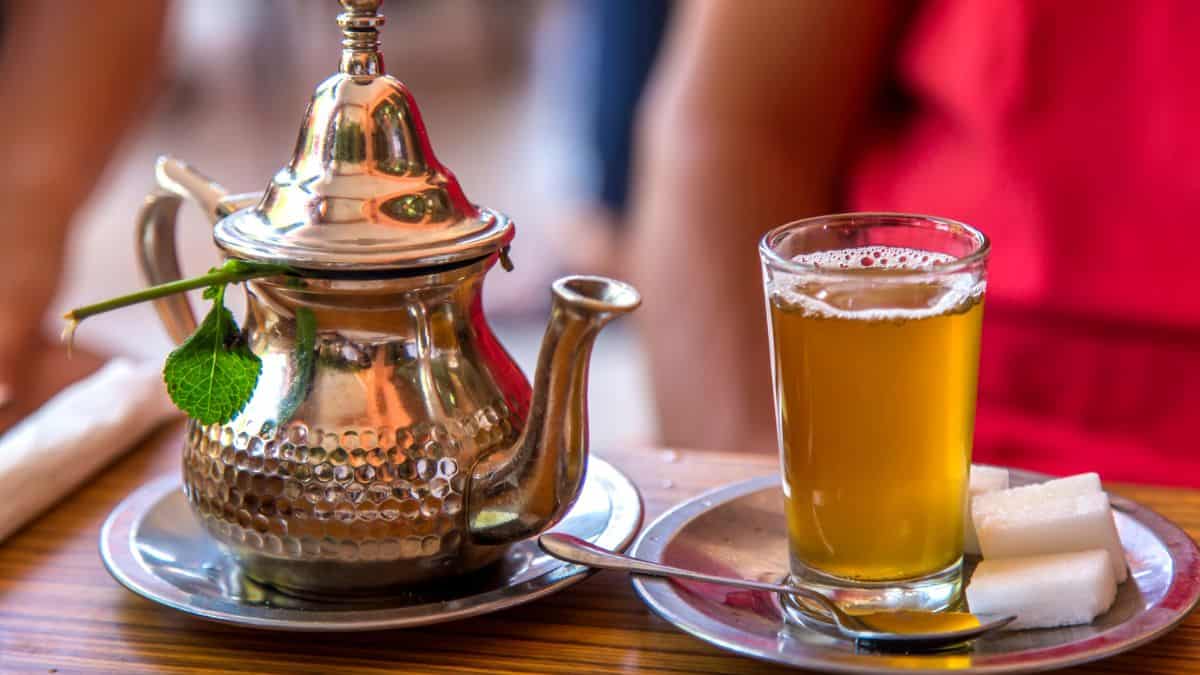 Moroccan mint tea in a cup with a traditional tea pot in the background.