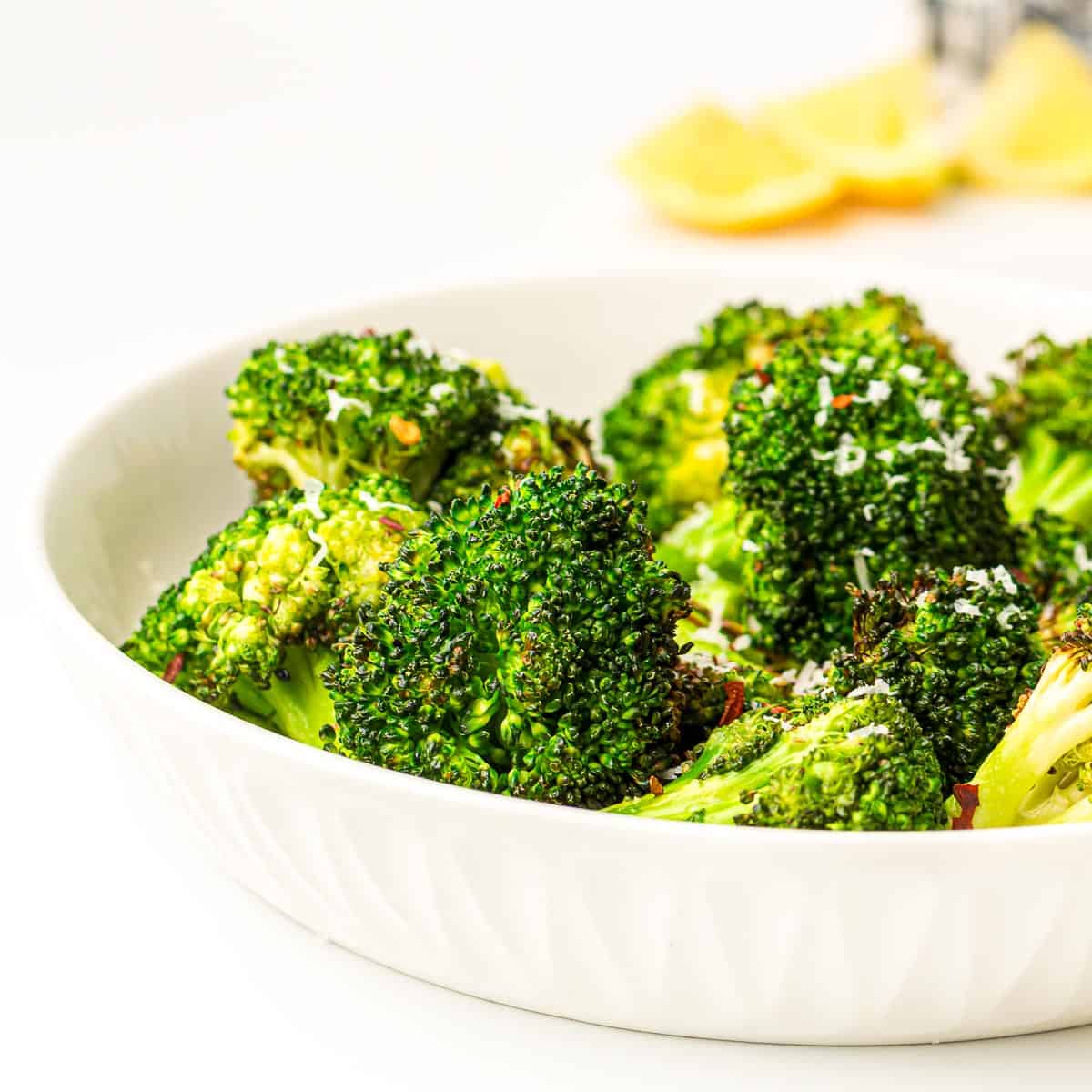 Side view of roasted broccoli in a white bowl.