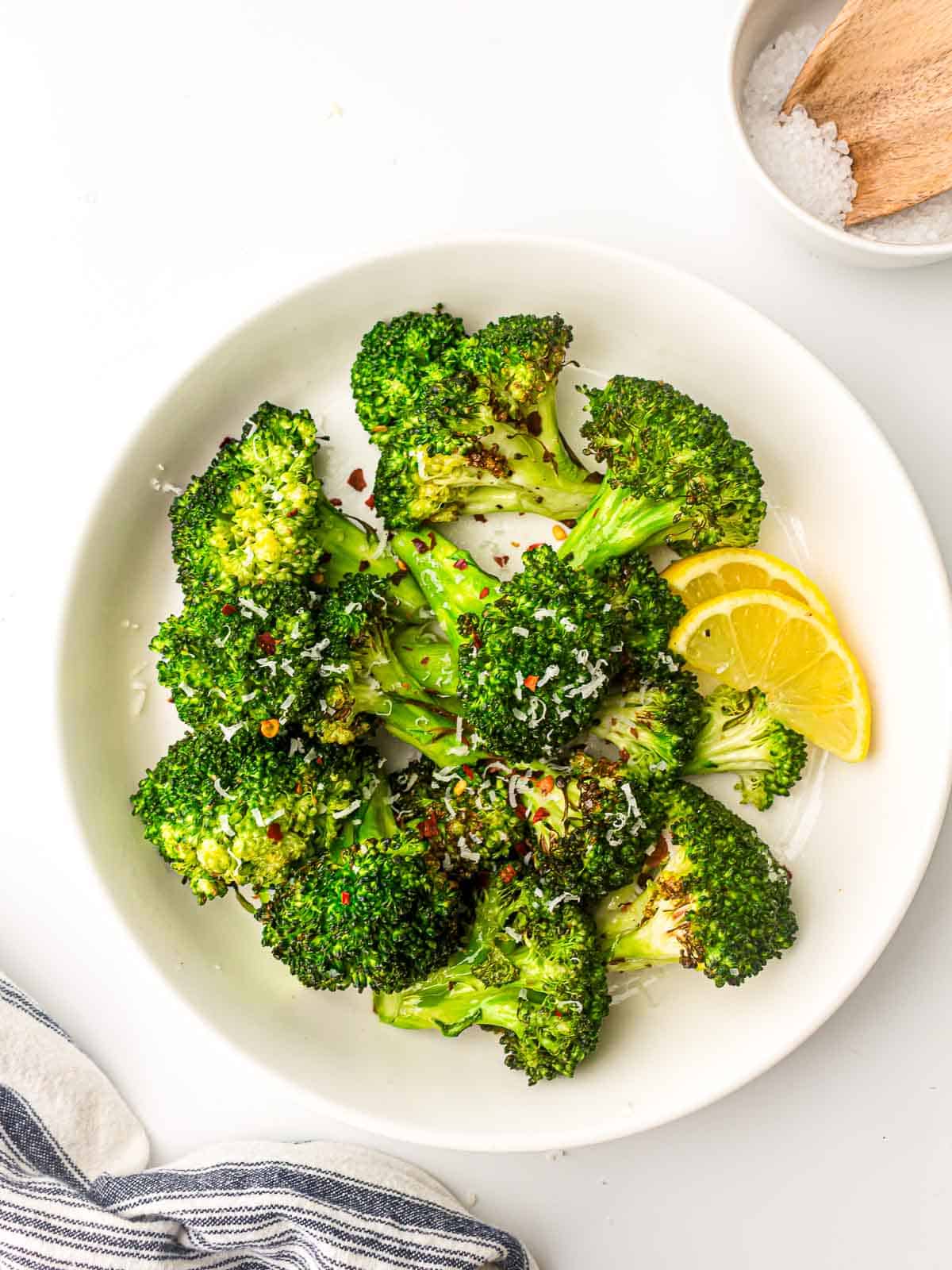 Air fryer broccoli on a white place garnished with lemon wedges.