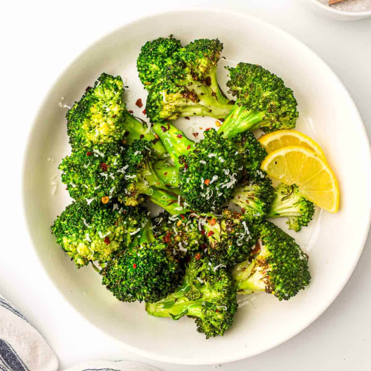 Air fryer broccoli on a white plate topped with chili flakes.